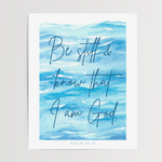 A vertical art print featuring a watercolor blue ocean scene with the hand-lettered quote 'Be still & know that I am God' and 'PSALM 46:10' at the bottom, shown against a light neutral background.