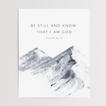 A minimalist art print featuring a watercolor mountain design in shades of gray and white, with the text 'BE STILL AND KNOW THAT I AM GOD' and 'PSALM 46:10' printed above the artwork on a white background.