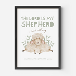 A framed personalized Christian art print featuring a watercolor illustration of a sheep with the text 'THE LORD IS MY SHEEPHERD', 'I lack nothing', and the name/date of the child