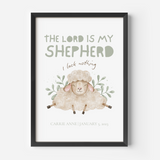 A framed personalized Christian art print featuring a watercolor illustration of a sheep with the text 'THE LORD IS MY SHEEPHERD', 'I lack nothing', and the name/date of the child