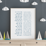 A framed Hebrew and English Bible print of psalm 23 displayed on a light wood dresser against a dark gray wall decorated with white paper clouds.